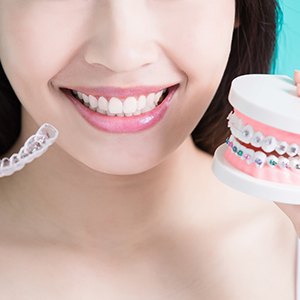 Woman holding Invisalign clear aligner and model with traditional braces