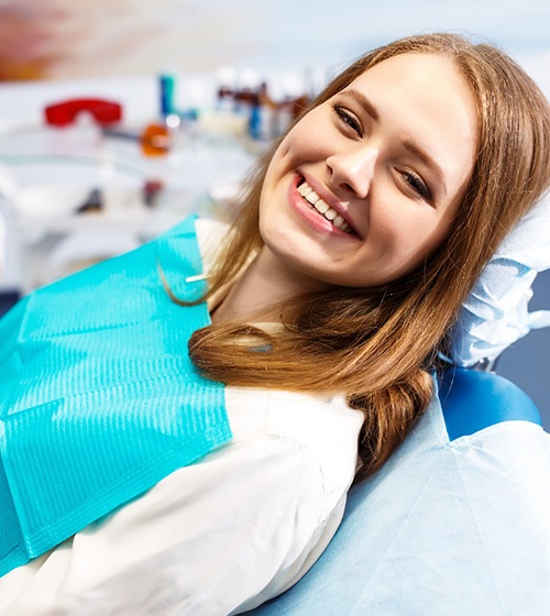 A female patient lying back in a dentist’s chair and smiling while seeing her orthodontist in Richardson