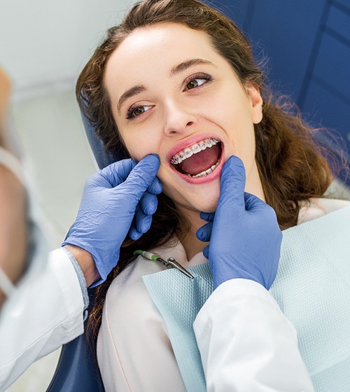 A dentist performing a checkup on a female patient who is wearing braces