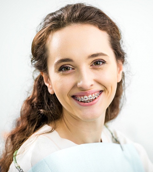 A young female with dark, curly hair smiling while seating in the dentist’s chair preparing to have her braces removed