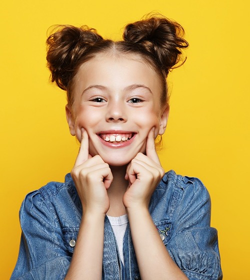 Happy young girl against yellow background, showing her smile