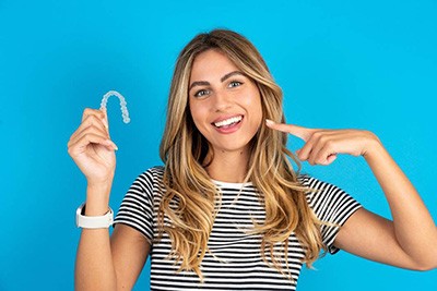 Woman holding Invisalign aligner, pointing at her teeth