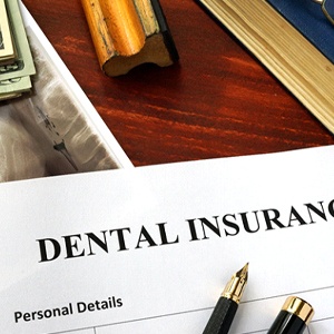 A paper that reads “Dental Insurance” with x-rays, pens, money, and a book lying nearby in Richardson
