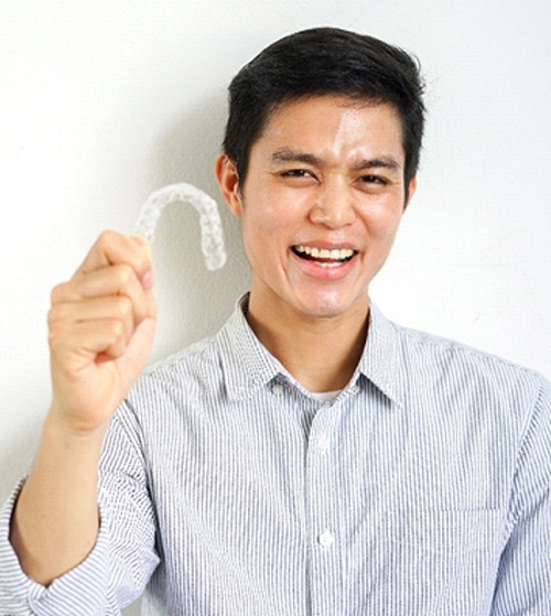 A male teenager wearing a button-down shirt and holding a clear Invisalign aligner
