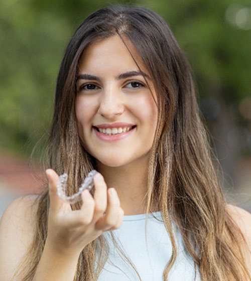 A young female teenager wearing her hair down and preparing to insert an Invisalign aligner into her mouth