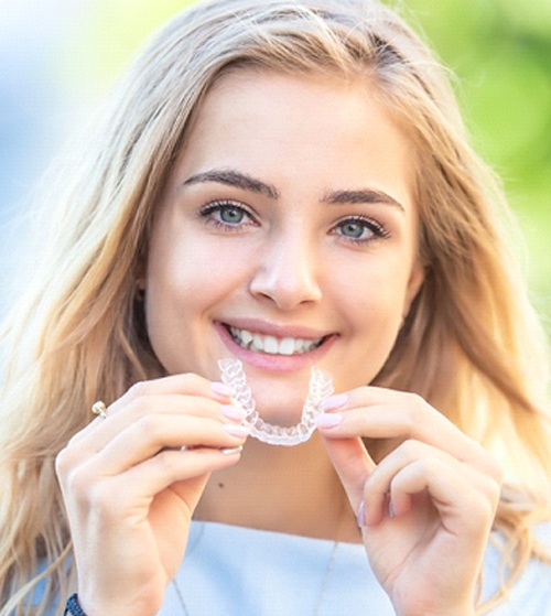 A female teenager smiling and inserting a clear aligner into her mouth after eating