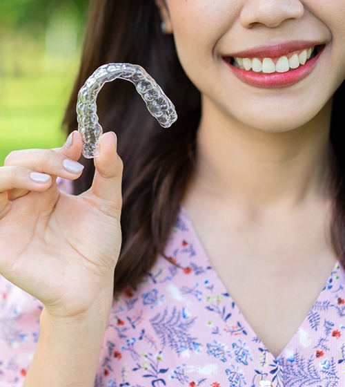 Happy Invisalign patient standing outside, holding well-made aligner