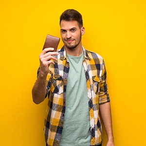 Man holding wallet against yellow background, ready to pay for orthodontic treatment