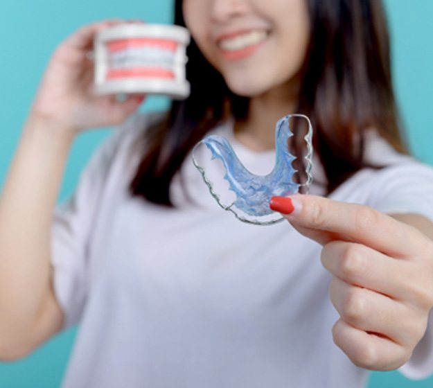Smiling patient holding blue orthodontic retainer