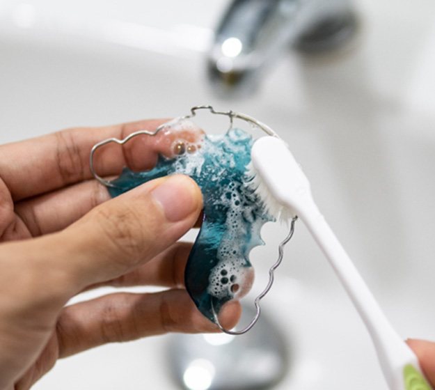 Patient using toothbrush to clean blue retainer in sink