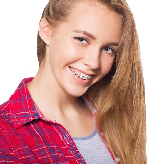 A female teenager wearing a red plaid button-down shirt and smiling while showing off her metal braces