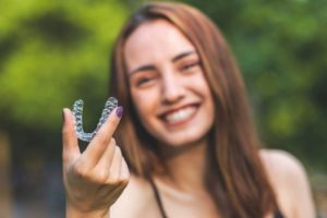 a woman smiling and holding her Invisalign aligner