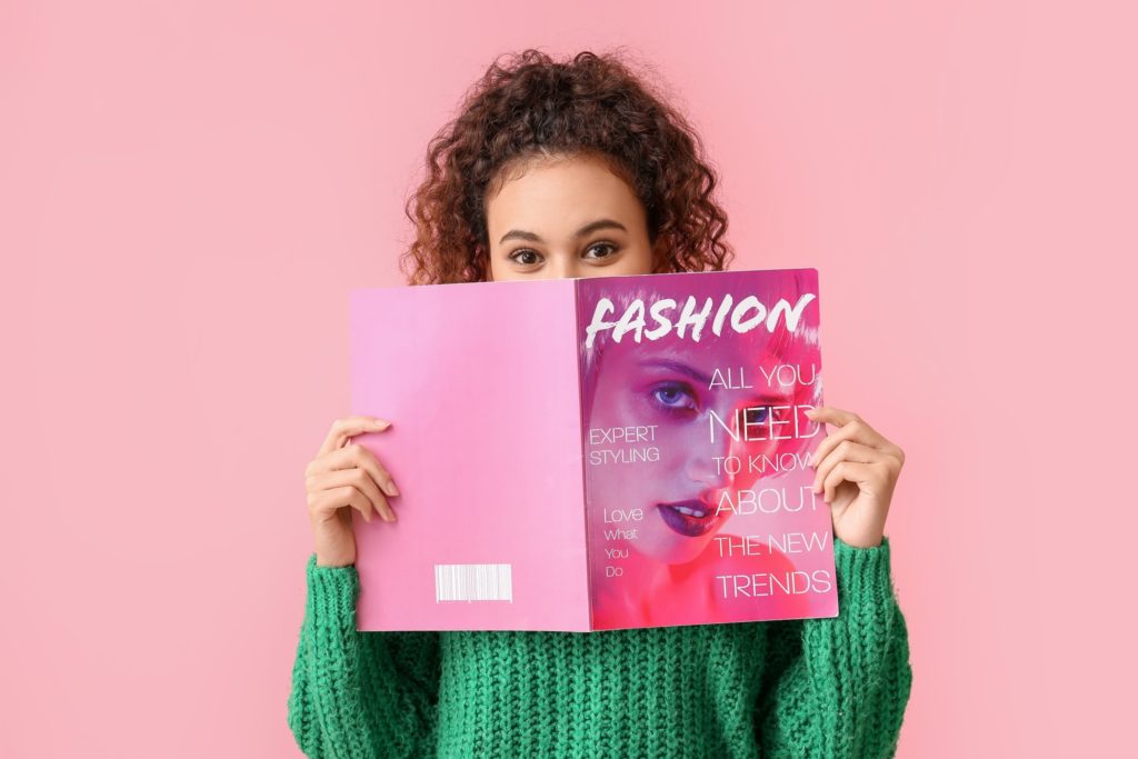 Patient in green sweater smiling behind pink fashion magazine