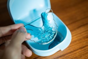 Hand holding retainer above its storage case