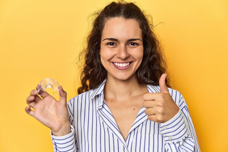 A woman smiling as she holds up her Invisalign aligner