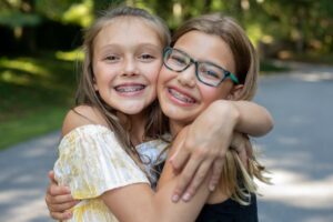 Two young girls with braces hugging and smiling. 